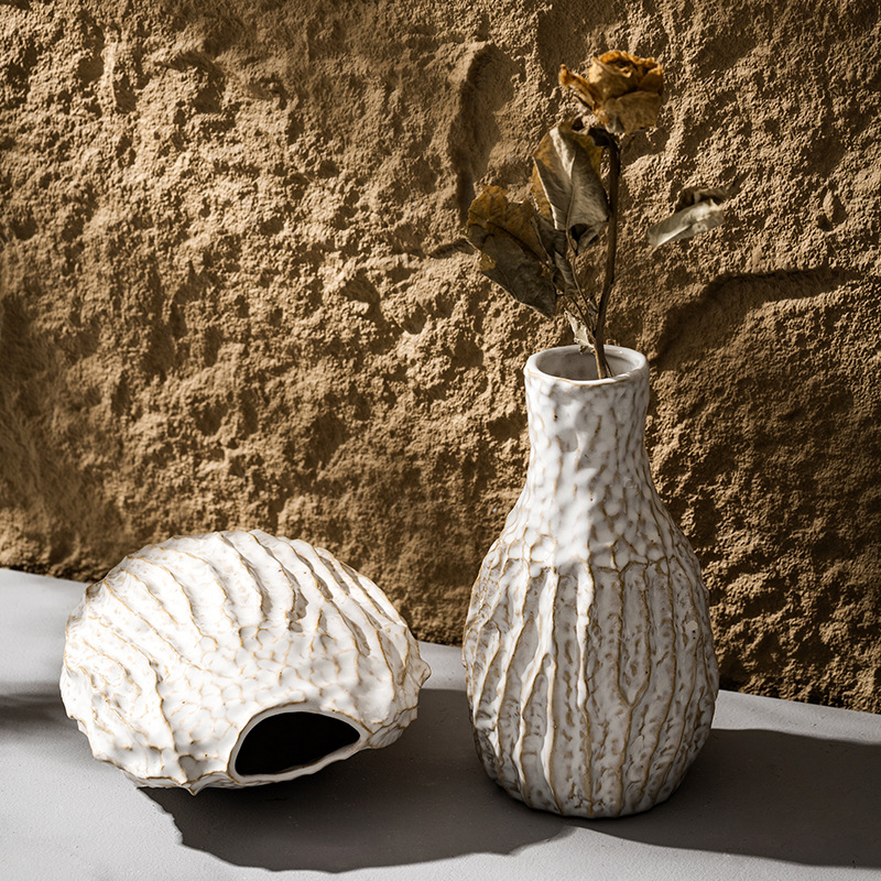 Textured ceramic vase with dried flowers against a textured wall.