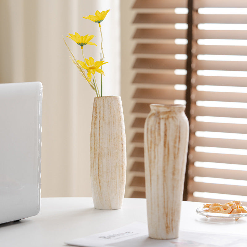 Two tall, cylindrical vases with a natural stone finish on a table with a blurred background.