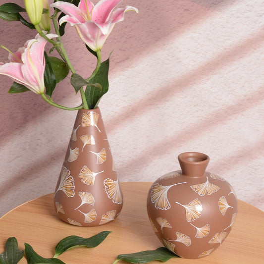 Two brown vases with floral patterns on a wooden surface with pink fabric in the background.