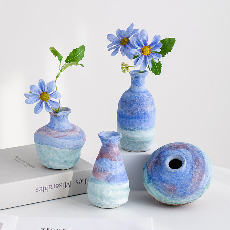 Set of small ceramic vases with blue and green glaze, each containing a flower, on a white surface.