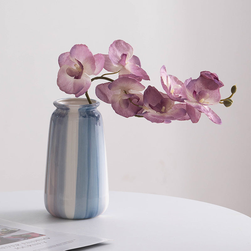 Striped vase with pink flowers on a white surface