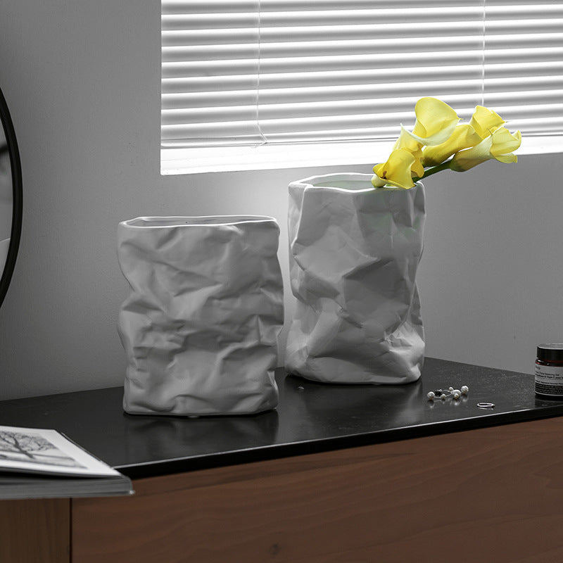 Two textured vases on a surface with one containing yellow flowers.