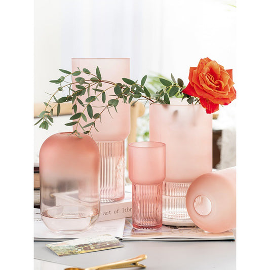 Set of pink glass vases and glasses with flowers on a white surface