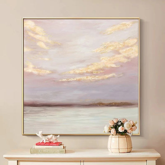 Framed artwork of a sunset over water on a wall above a table with decor items.