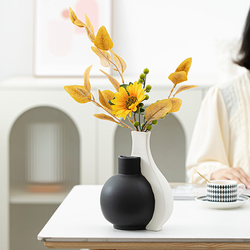 Two vases, one black and one white, with a sunflower arrangement on a table.