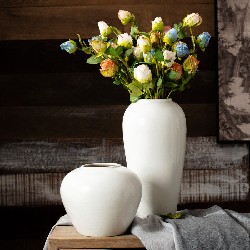 Two white vases with a bouquet of flowers on a wooden surface against a wooden wall.