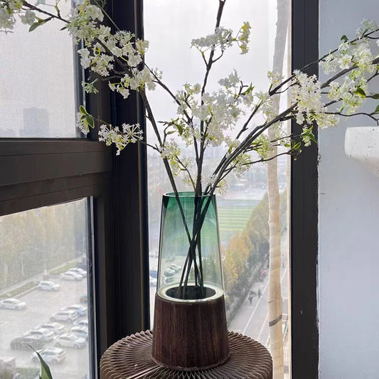 Decorative vase with white flowers on a windowsill with a cityscape view.