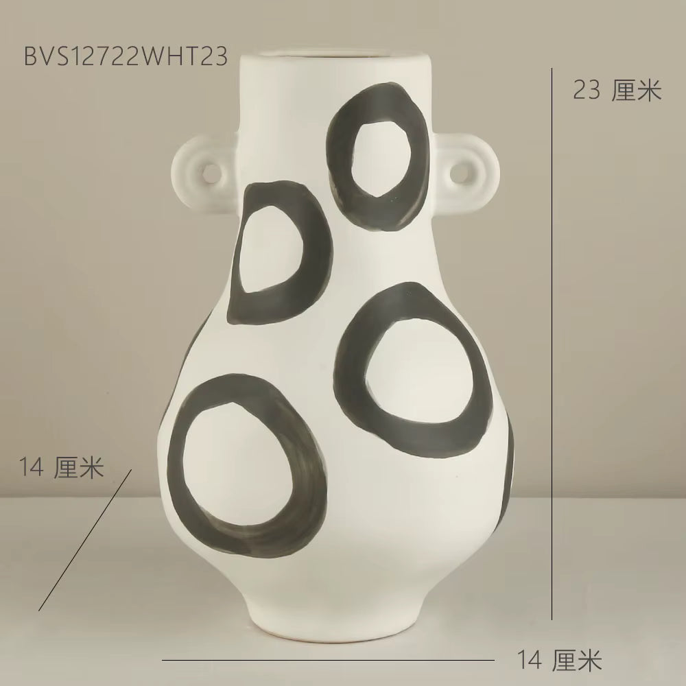 White vase with black circular patterns on a neutral background