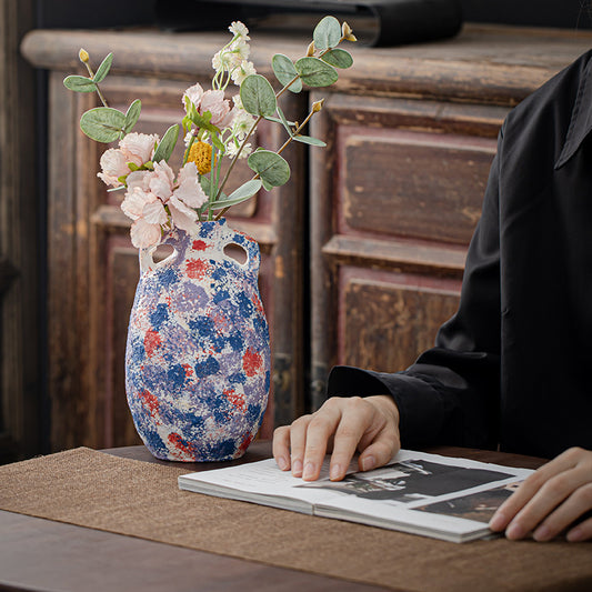Decorative vase with flowers on a table next to a person翻阅相册