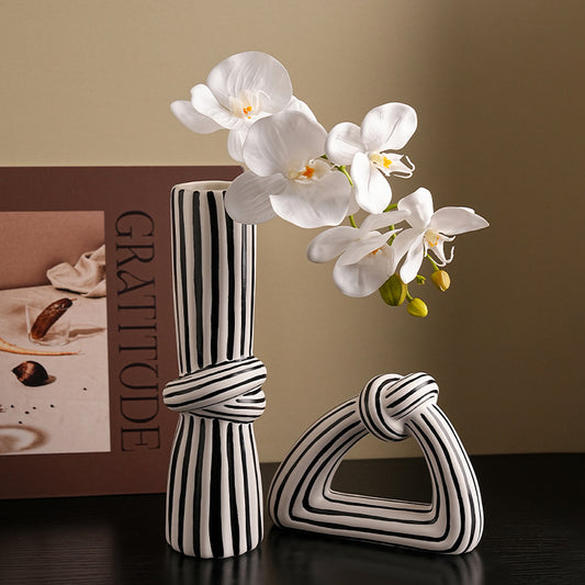 Black and white striped vases with a bouquet of white orchids on a dark surface.