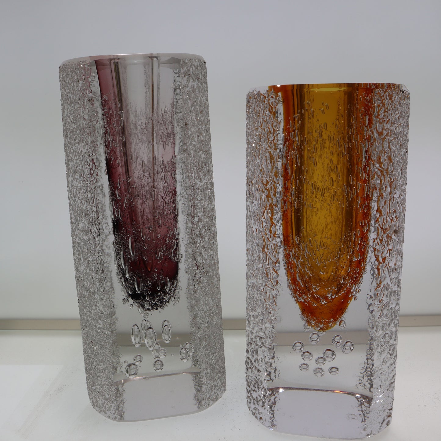 Two textured glass vases with one having a purple tint and the other an orange tint on a white background.