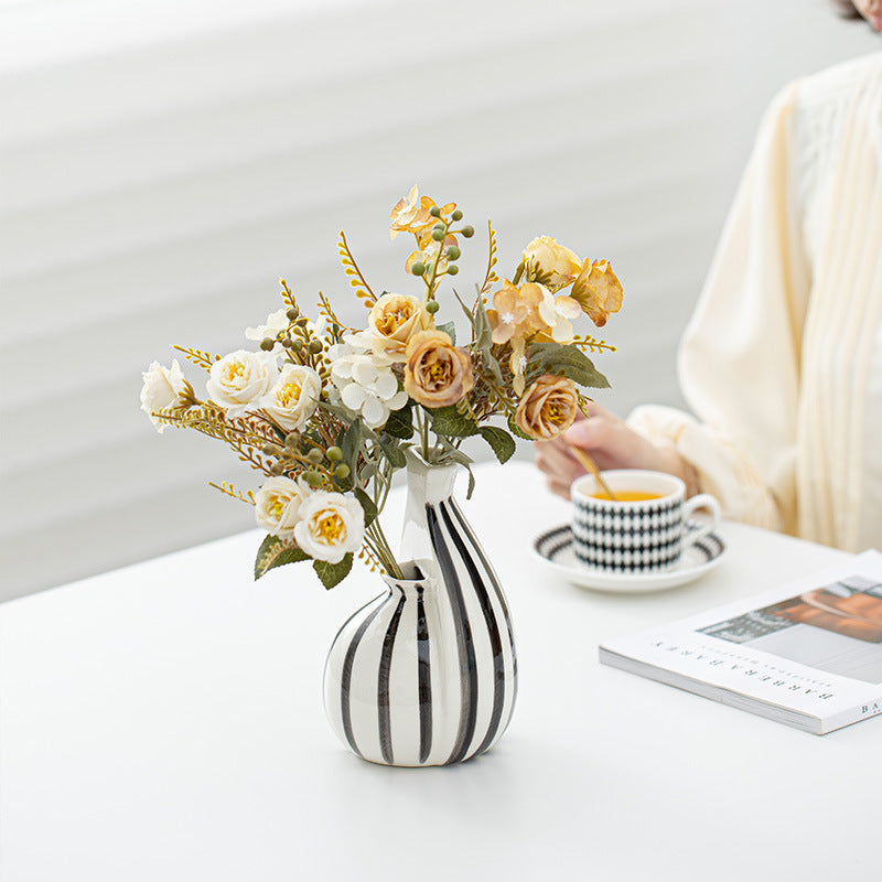 Striped vase with flowers on a table next to a cup of coffee and a book.
