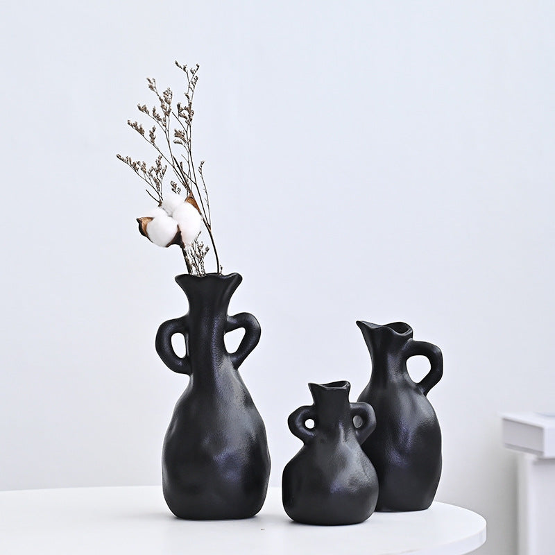 Three black vases of different sizes on a white surface with a light gray background