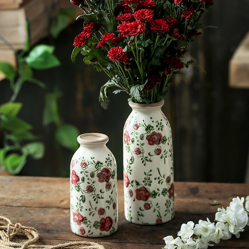 Two decorative ceramic bottles with floral patterns on a wooden surface, surrounded by flowers.