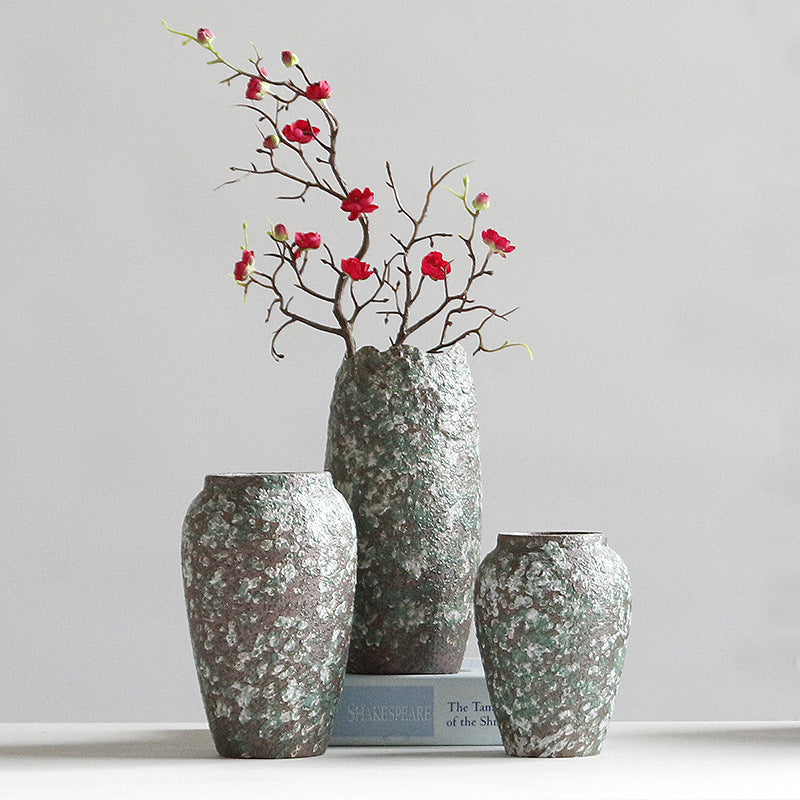 Three textured vases with a branch of red flowers on a light gray background