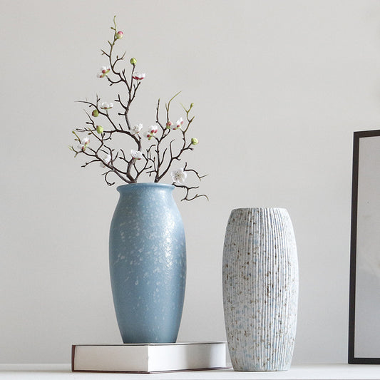 Two vases, one blue and one textured gray, on a white surface with a light gray wall background.