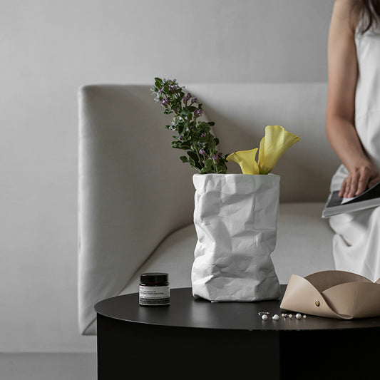 White paper bag with flowers on a black table against a gray wall
