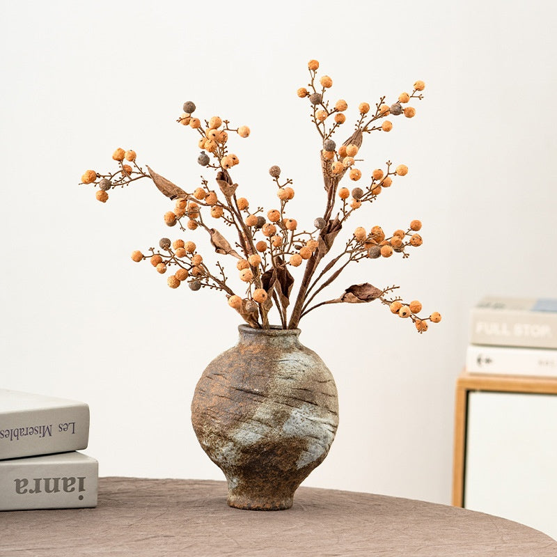 Decorative vase with branches and berries on a wooden surface