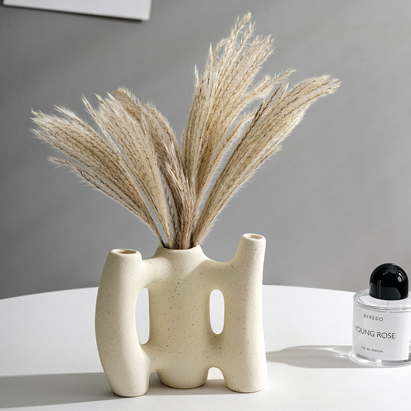 Ceramic vase with dried plants on a white surface with a gray background