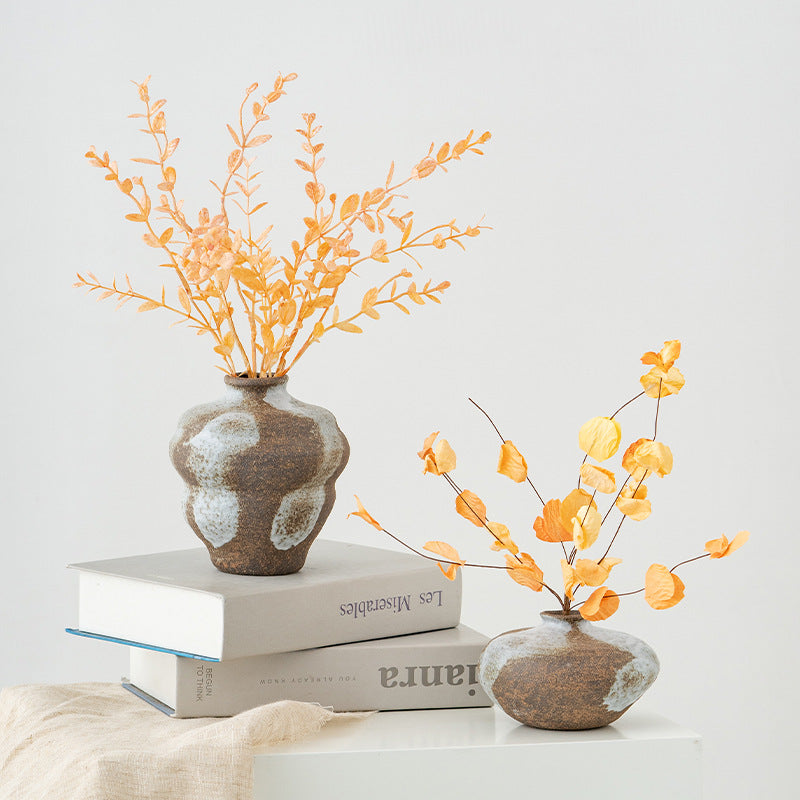Two small vases with orange branches on a white surface
