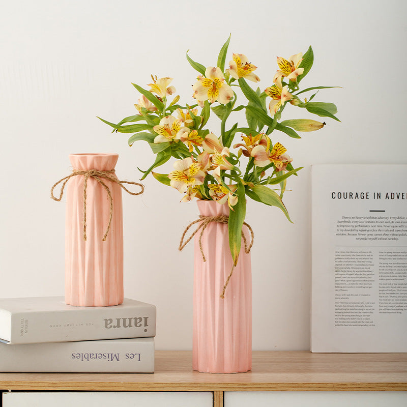 Two pink vases with floral arrangements on a wooden surface with books and a magazine in the background.