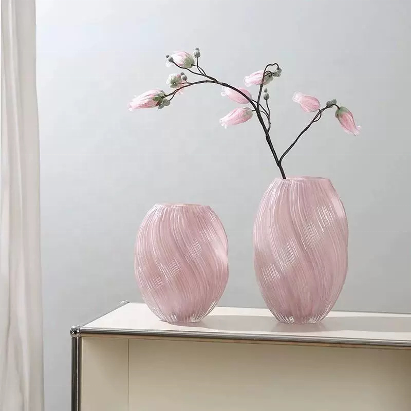 Two pink glass vases with a branch of flowers on a light surface against a light gray background.