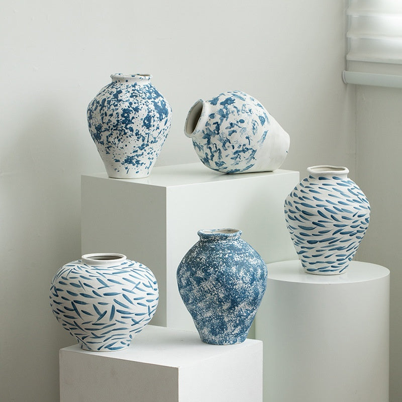 Set of five blue and white patterned vases on white pedestals against a light gray wall.