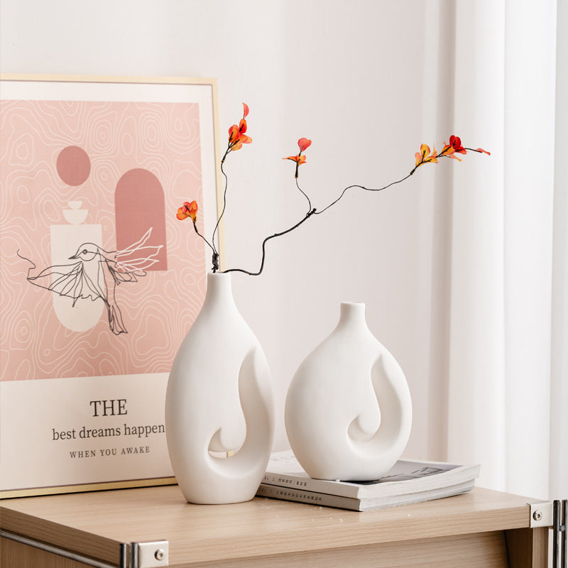 Two white vases with floral branches on a wooden surface with a pink poster in the background.