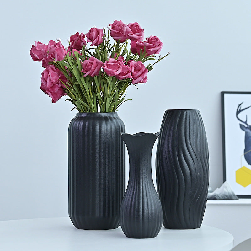 Three dark gray vases with a bouquet of pink roses on a light blue background