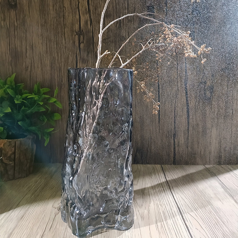 Decorative glass vase with textured surface on a wooden floor against a wooden wall.