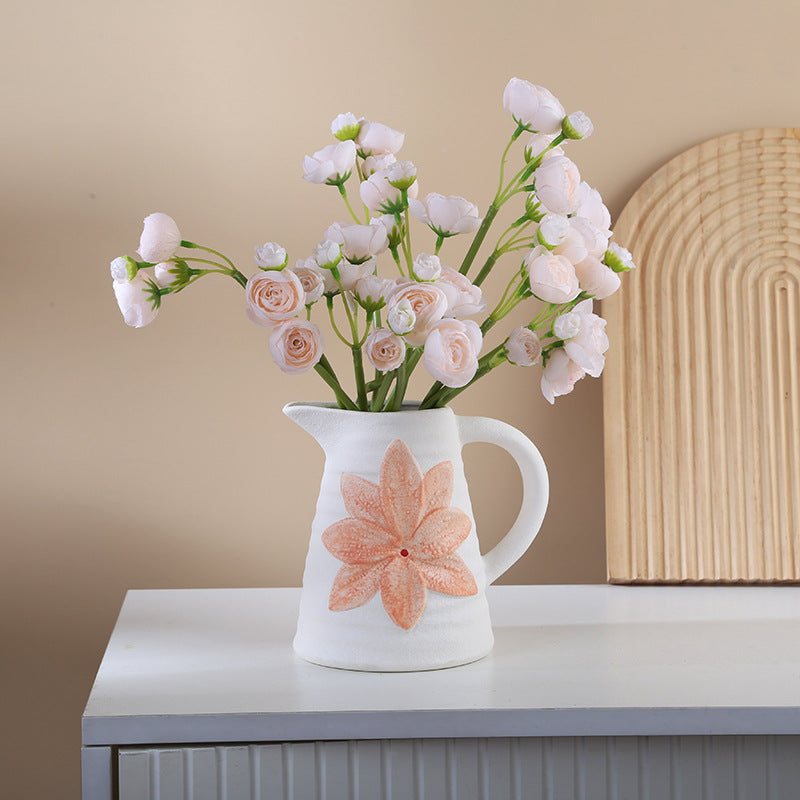 White pitcher with pink floral design holding flowers on a white surface with a beige wall background