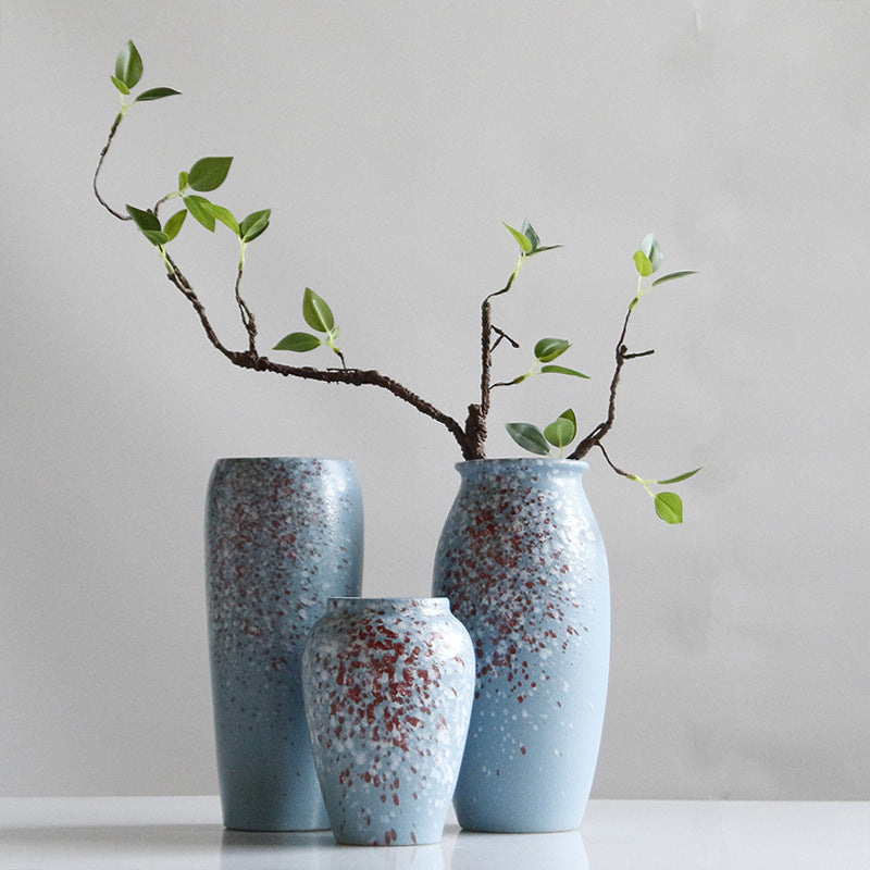 Three speckled blue vases with a branch on a plain background