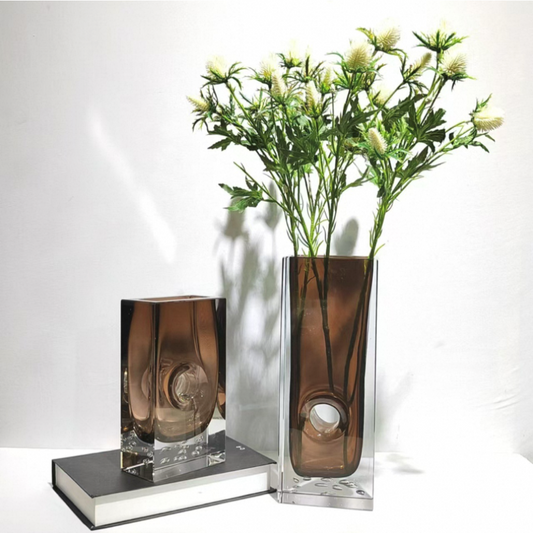 Two glass vases with one containing greenery on a white background
