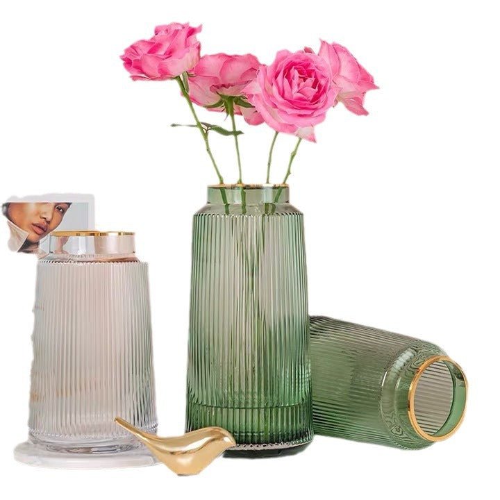 Green ribbed vase with pink roses, next to a white ribbed vase and gold spoon on a white background