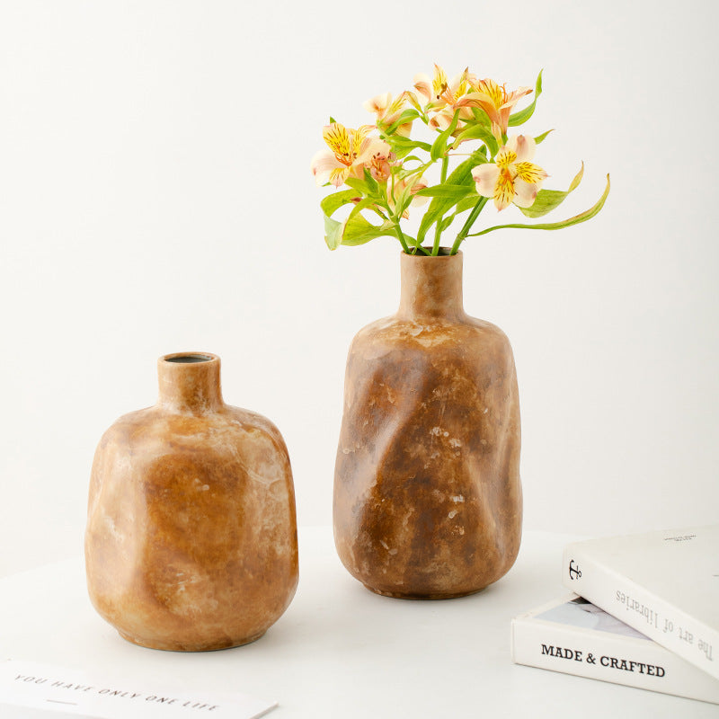 Two brown ceramic vases with a small bouquet of flowers on a white surface with books underneath.