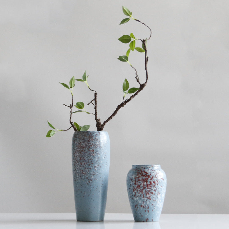 Two speckled blue vases with branches on a light gray background