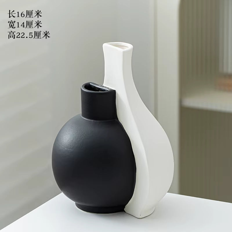Two ceramic vases, one black and one white, on a light surface with a neutral background.