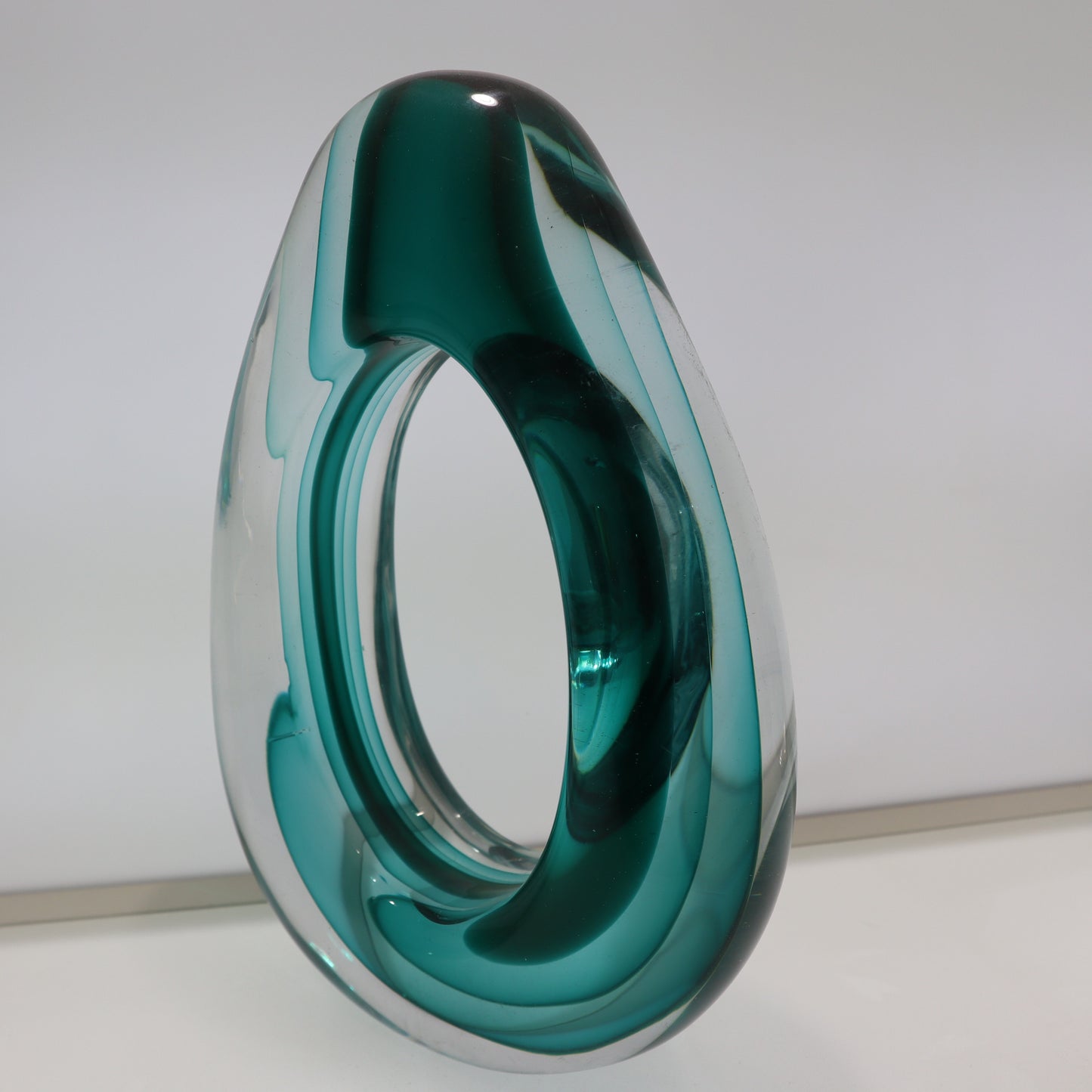 Teal and clear glass sculpture on a white background