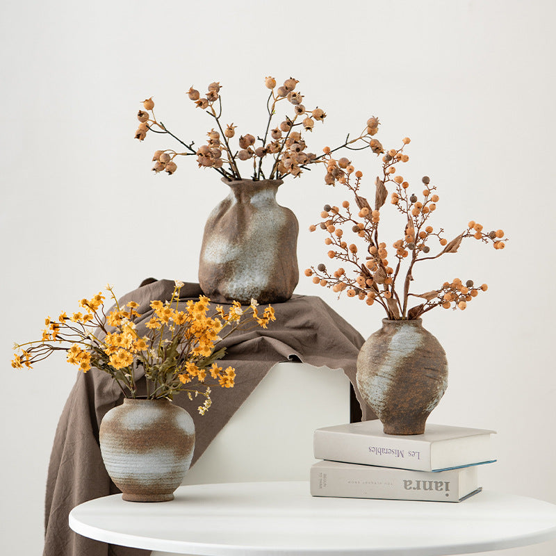 Three ceramic vases with dried flowers on a white surface