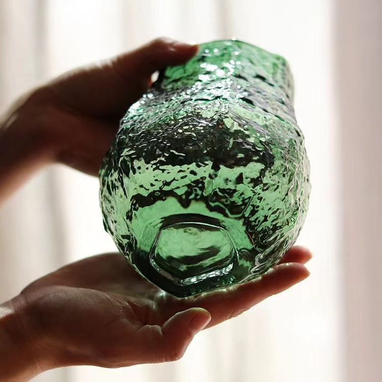 Green glass vase held in hands with a blurred background