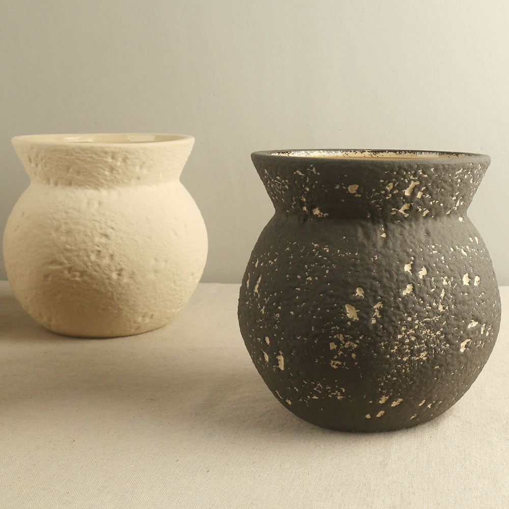 Two ceramic vases, one white and one black speckled, on a neutral background