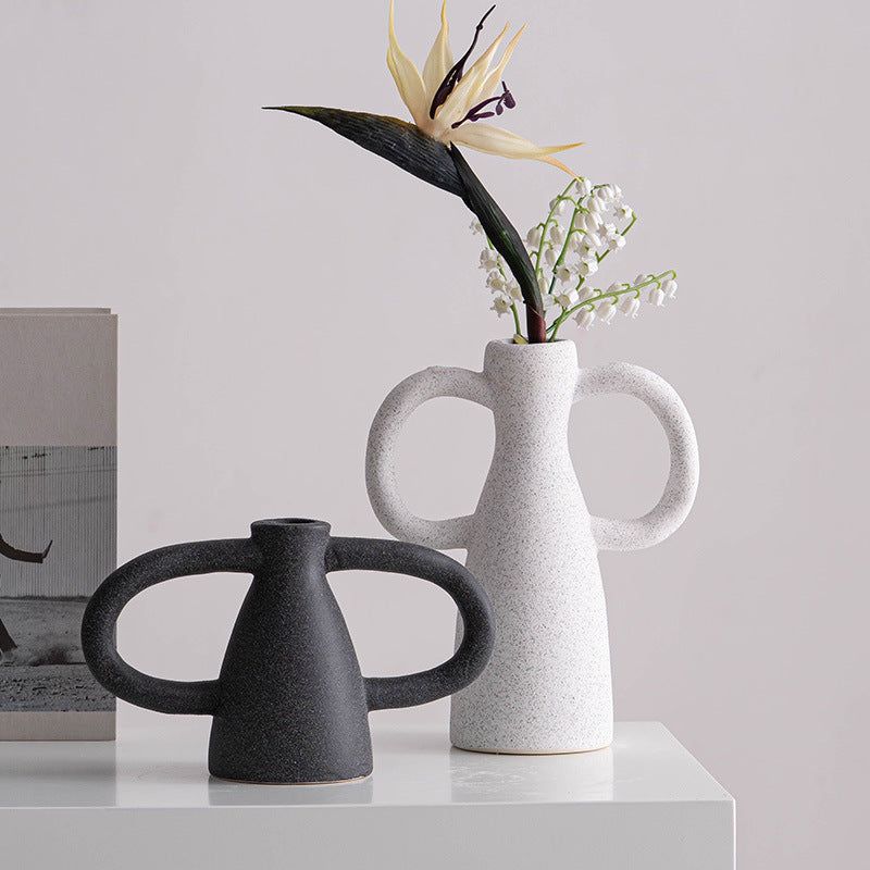 Two ceramic vases, one black and one white with handles, on a light surface with a neutral background.
