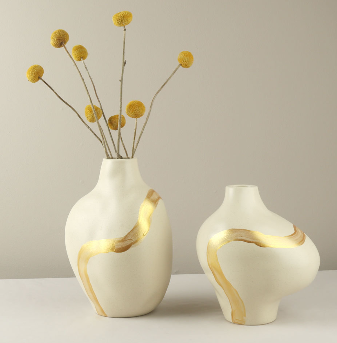 Two white vases with gold accents on a neutral background