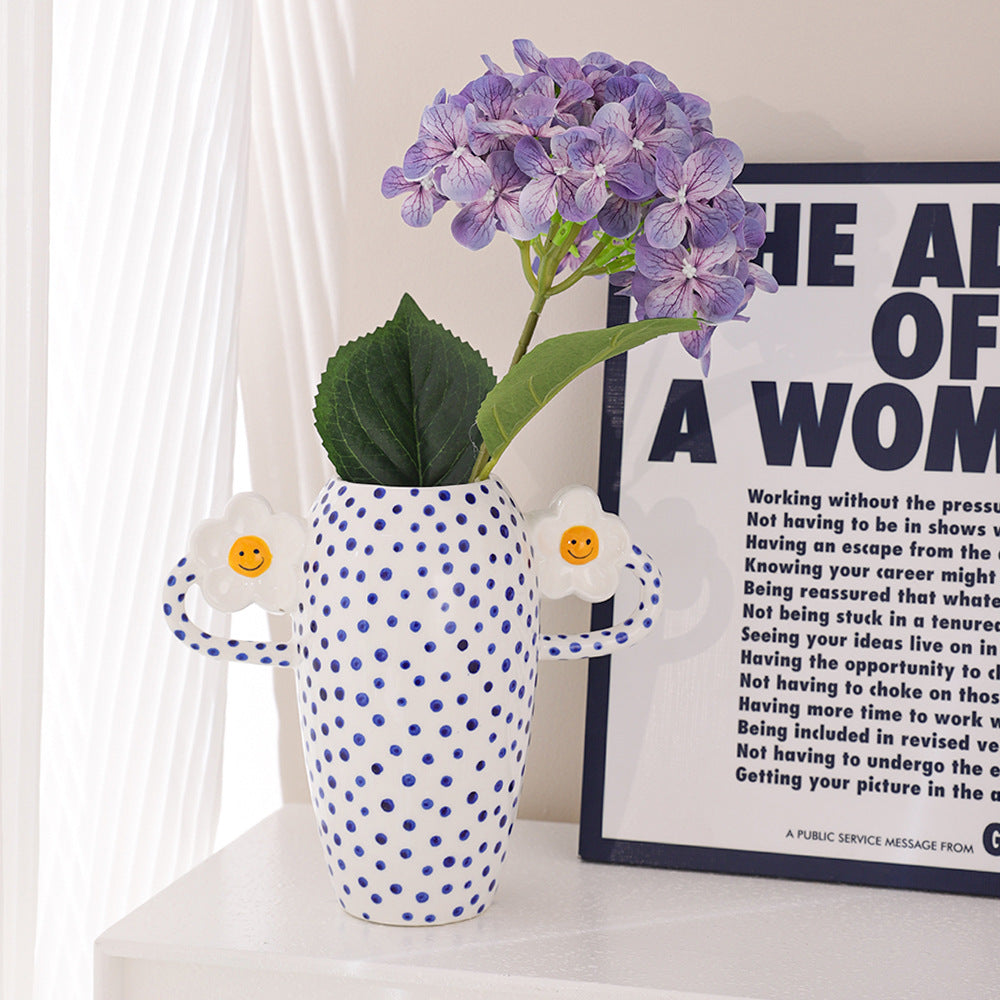 Polka dot vase with purple flowers on a shelf next to a framed text poster.