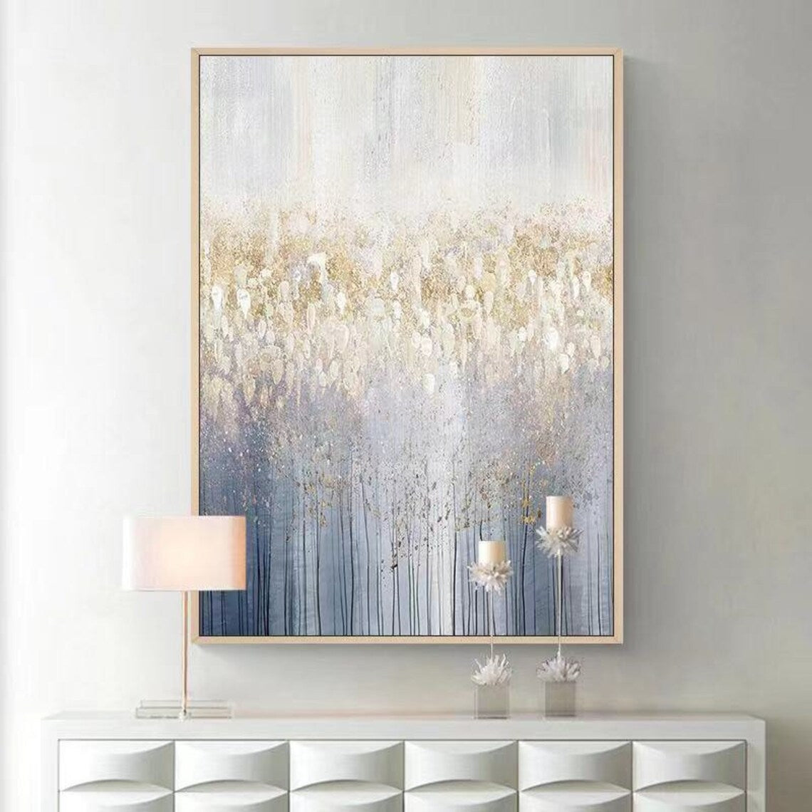 Abstract painting with gold and blue tones on a gray wall above a white console table.