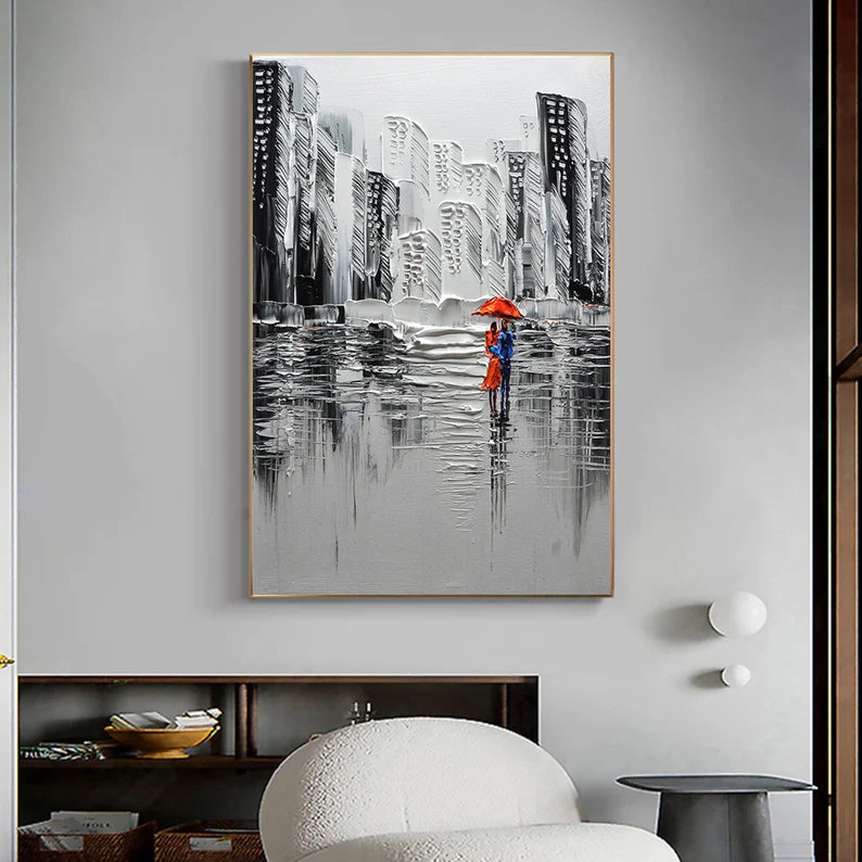 Framed artwork of a cityscape with two people holding a red umbrella, hanging on a wall.