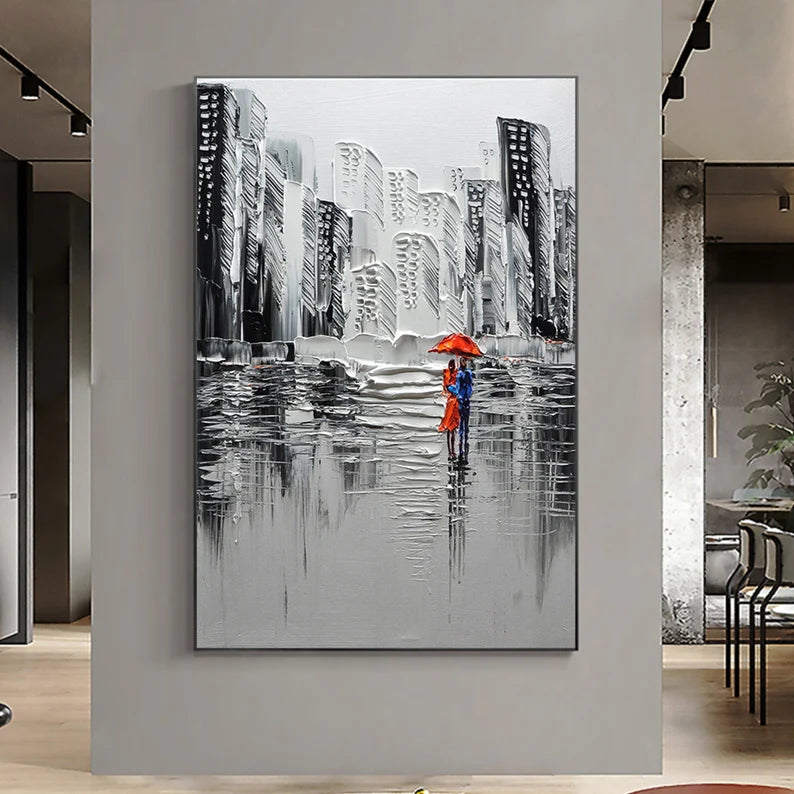 Framed artwork of a couple with an orange umbrella against a cityscape background, displayed on a wall.