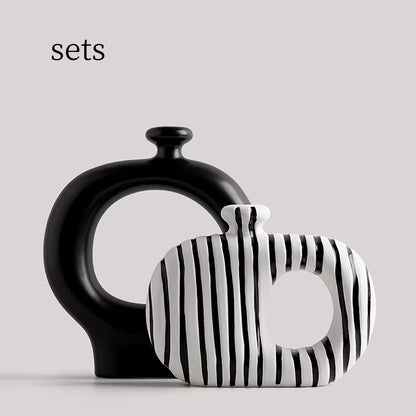 Two ceramic vases, one black and one with black and white striped pattern, on a light gray background.