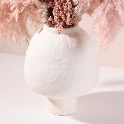 White vase with pink flowers against a soft pink background