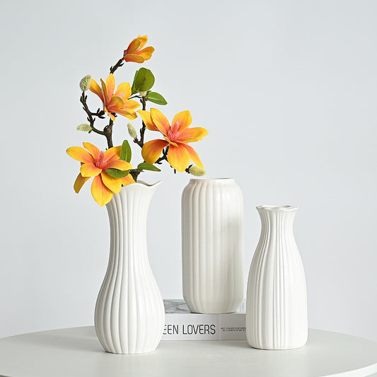 Three white vases of different shapes on a light gray background with a vase containing orange flowers.